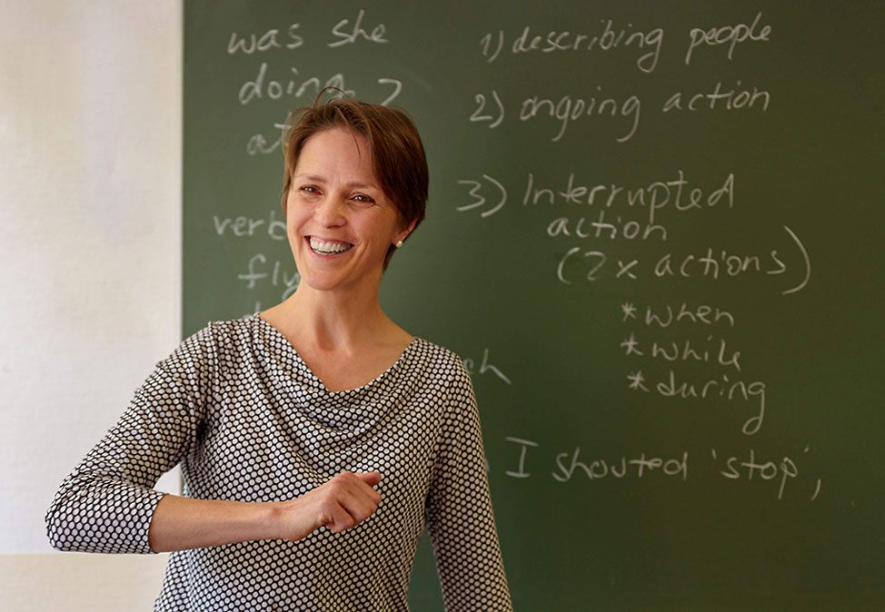 A teacher in an English course at DIE NEUE SCHULE Sprachschule Berlin in front of a green board with English vocabulary
