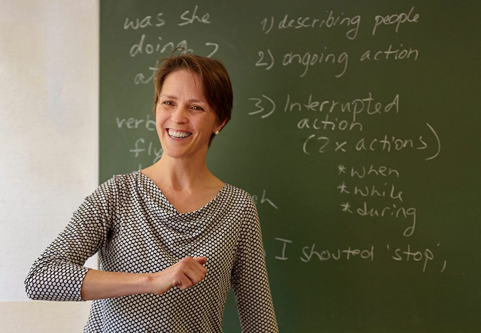 Eine Lehrerin in einem Englischkurs von DIE NEUE SCHULE Sprachschule Berlin vor einer grünen Tafel mit englischen Vokabeln.