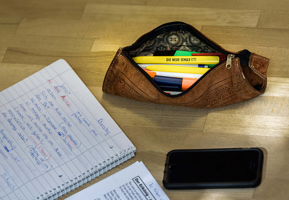 Sur une table se trouvent un carnet d'écriture, un téléphone et des stylos de la DIE NEUE SCHULE Sprachschule Berlin.